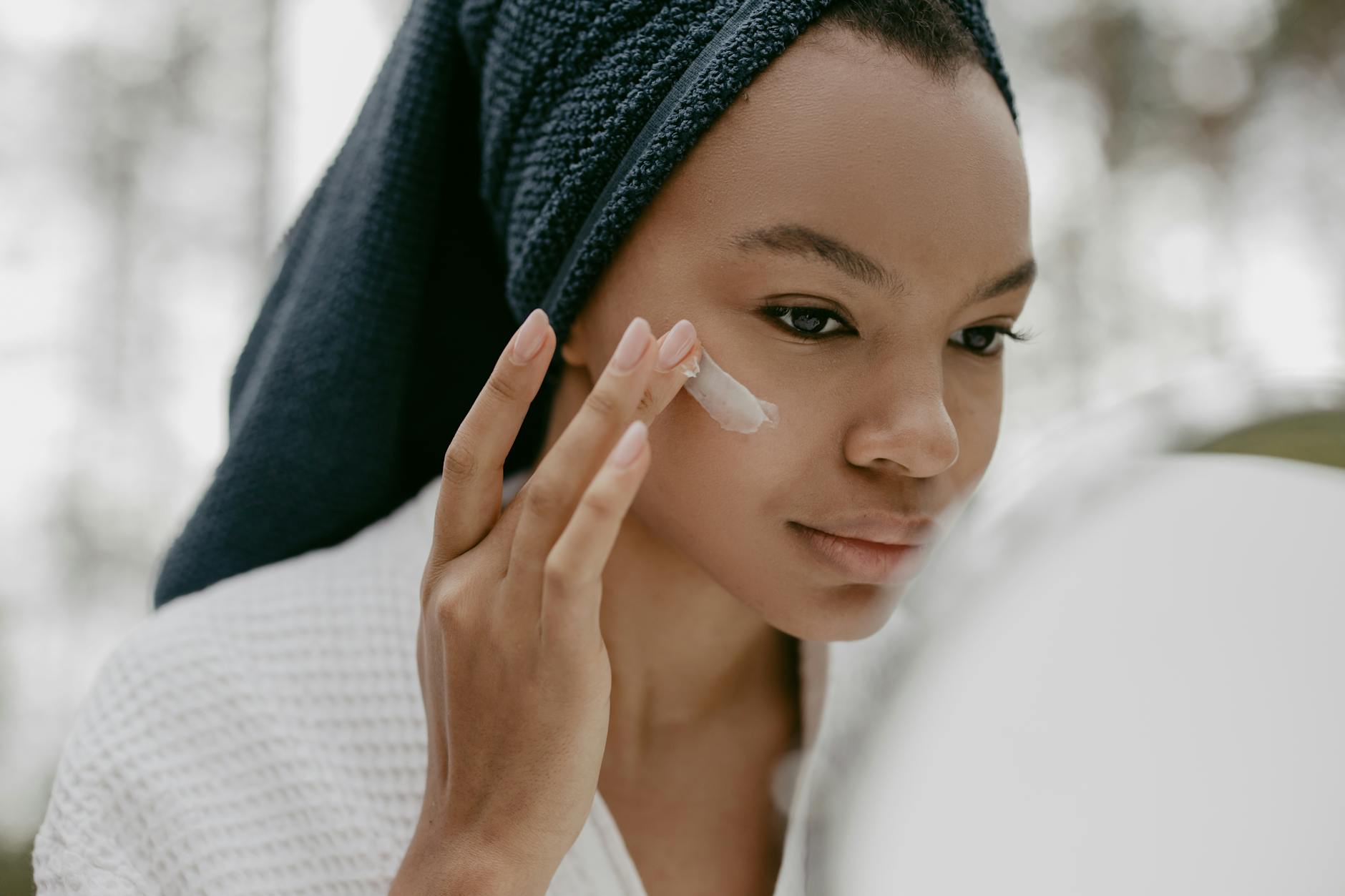 woman wearing bathrobe putting facial cream