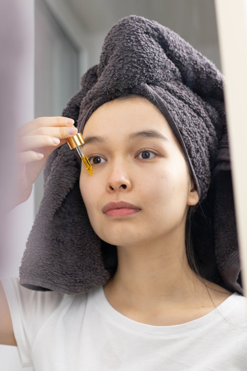 woman with gray bath towel on her head applying a face serum